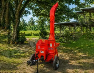 Bright red portable wood chipper on a trailer in a sunny yard with trees and a shed nearby.