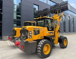 Yellow wheel loader with a large raised front bucket parked outside a modern gray industrial building, labeled MASSIVE on the cab and boom.