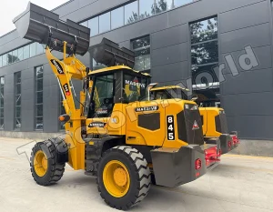 Large yellow wheel loader with raised front bucket parked outside a dark gray industrial building, branding visible on the machine.